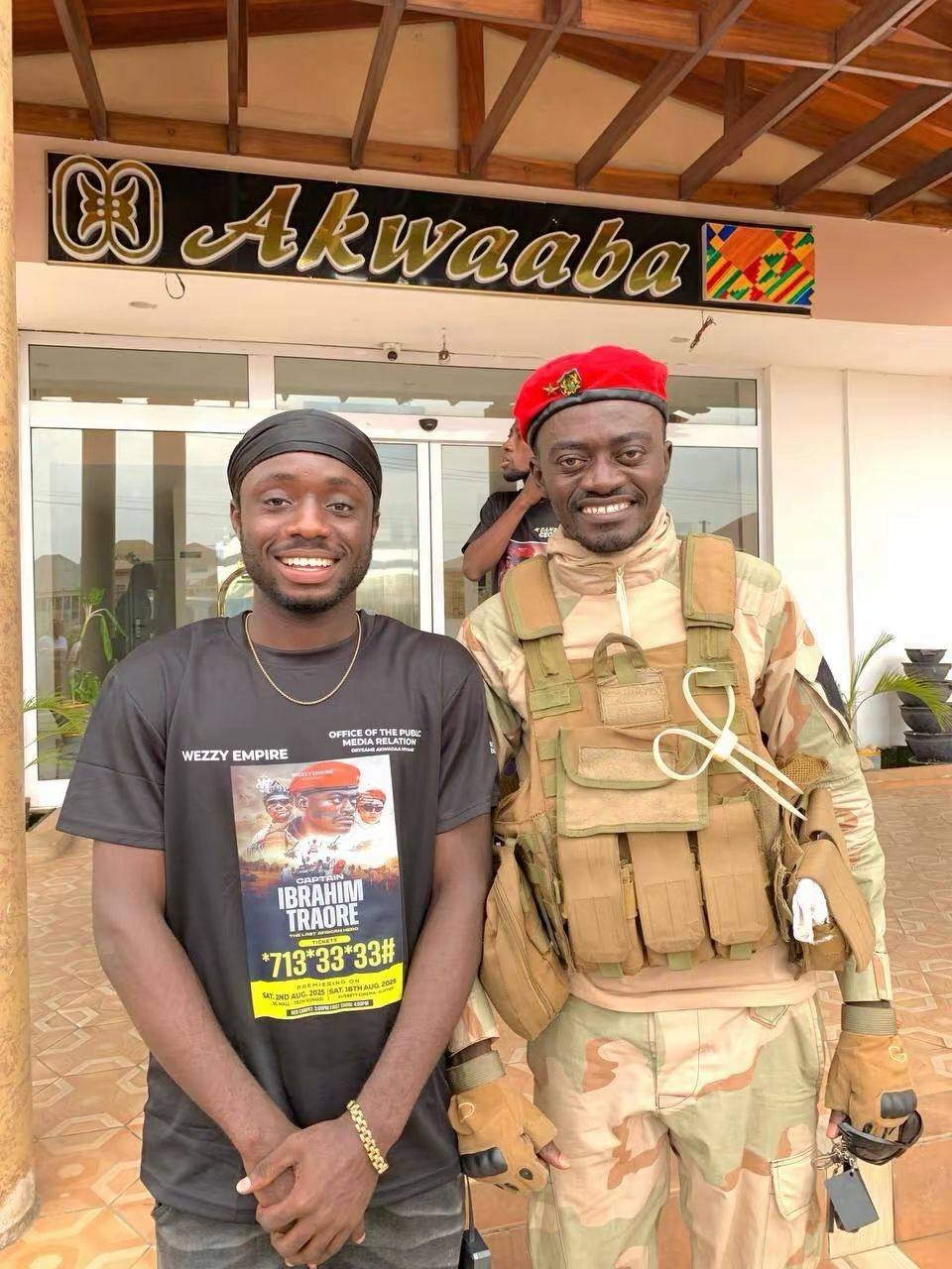 A smiling man in a black shirt standing beside a man dressed in a red beret and military clothing, outside a building